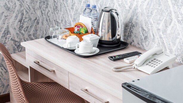 A hotel room with a wooden desk, a telephone, a tray with cups and a kettle, and a chair. - Manifa Hotel (Tashkent)