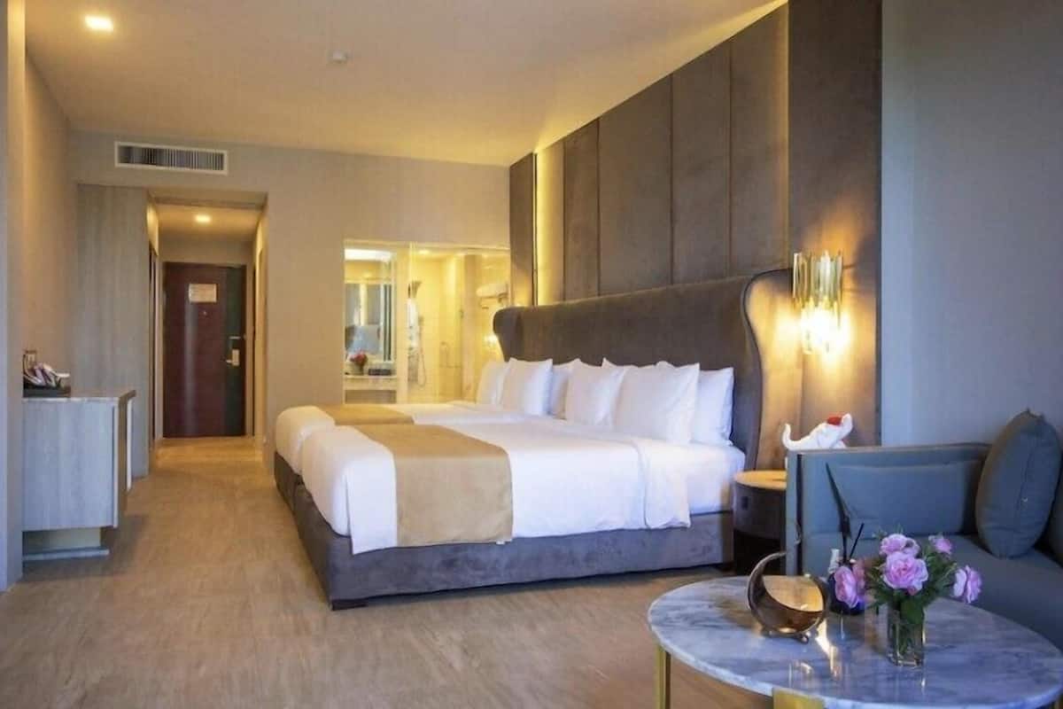 Ein Hotelzimmer mit einem großen Bett, einem Sofa, einem kleinen Tisch mit Blumen und einem Spiegel.