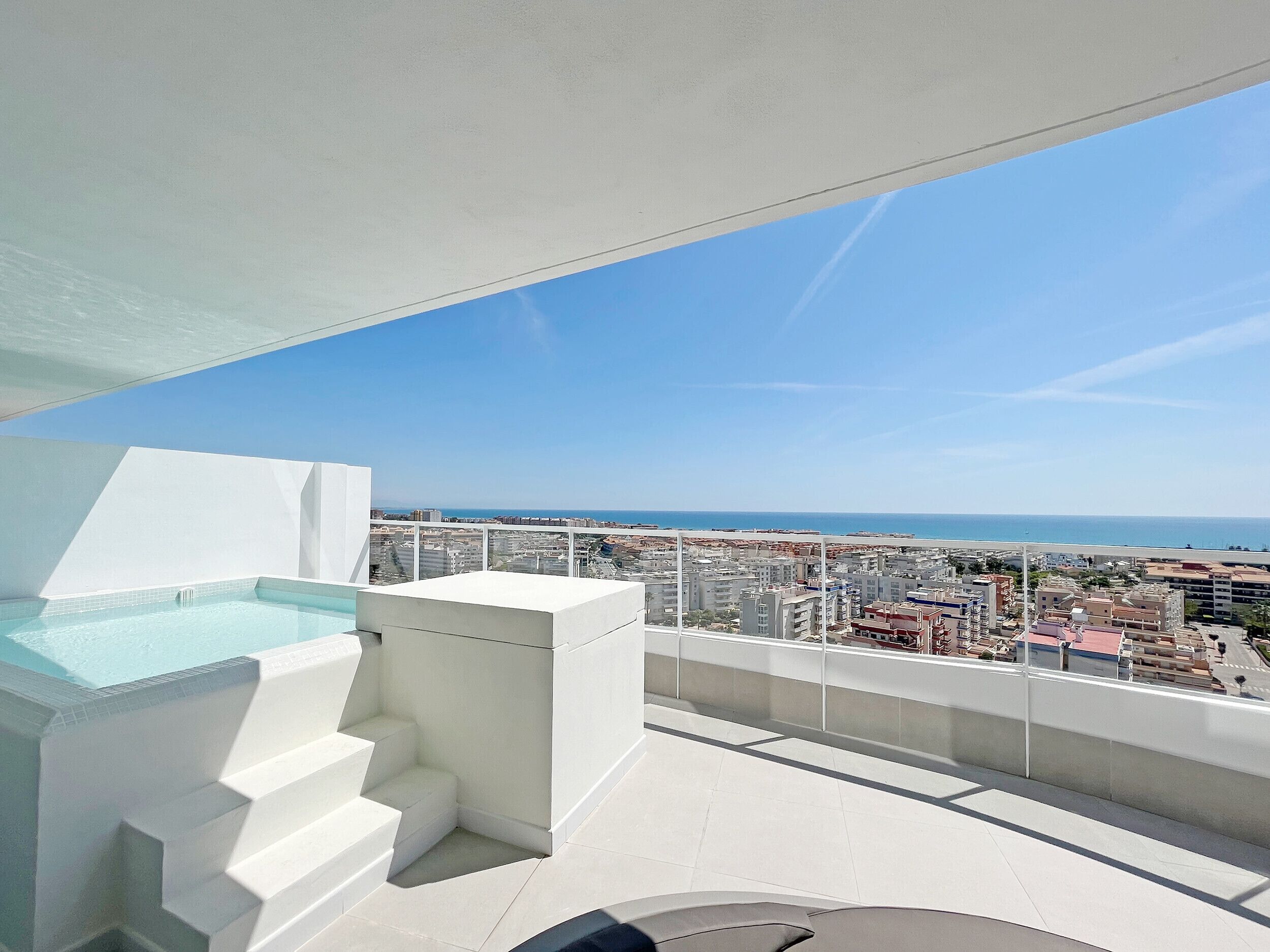 Una terraza en la azotea con piscina, una escalera y vistas a la ciudad y al mar.