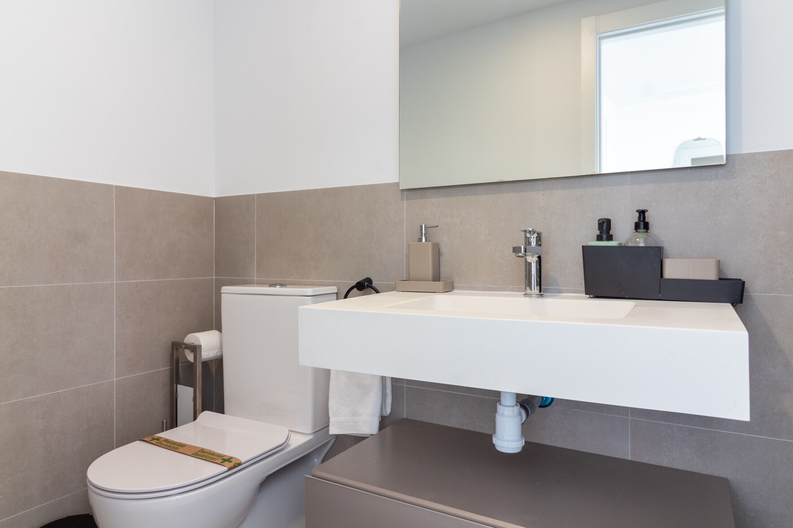 A modern bathroom with a white sink, a toilet, and a mirror above the sink.