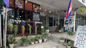 A storefront with a variety of plants and a signboard advertising coffee and beverages. - Chan&Both guesthouse (Sihanoukville)