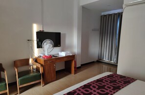 A hotel room with a wooden desk, a chair, a TV, a fan, and a window with curtains. - Chan&Both guesthouse (Sihanoukville)
