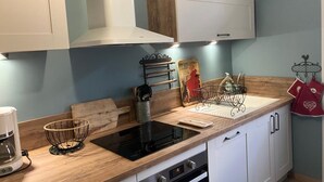 Una cocina moderna con armarios blancos, encimera de madera, placa de inducción negra, cafetera y un tendedero con toallas de cocina.