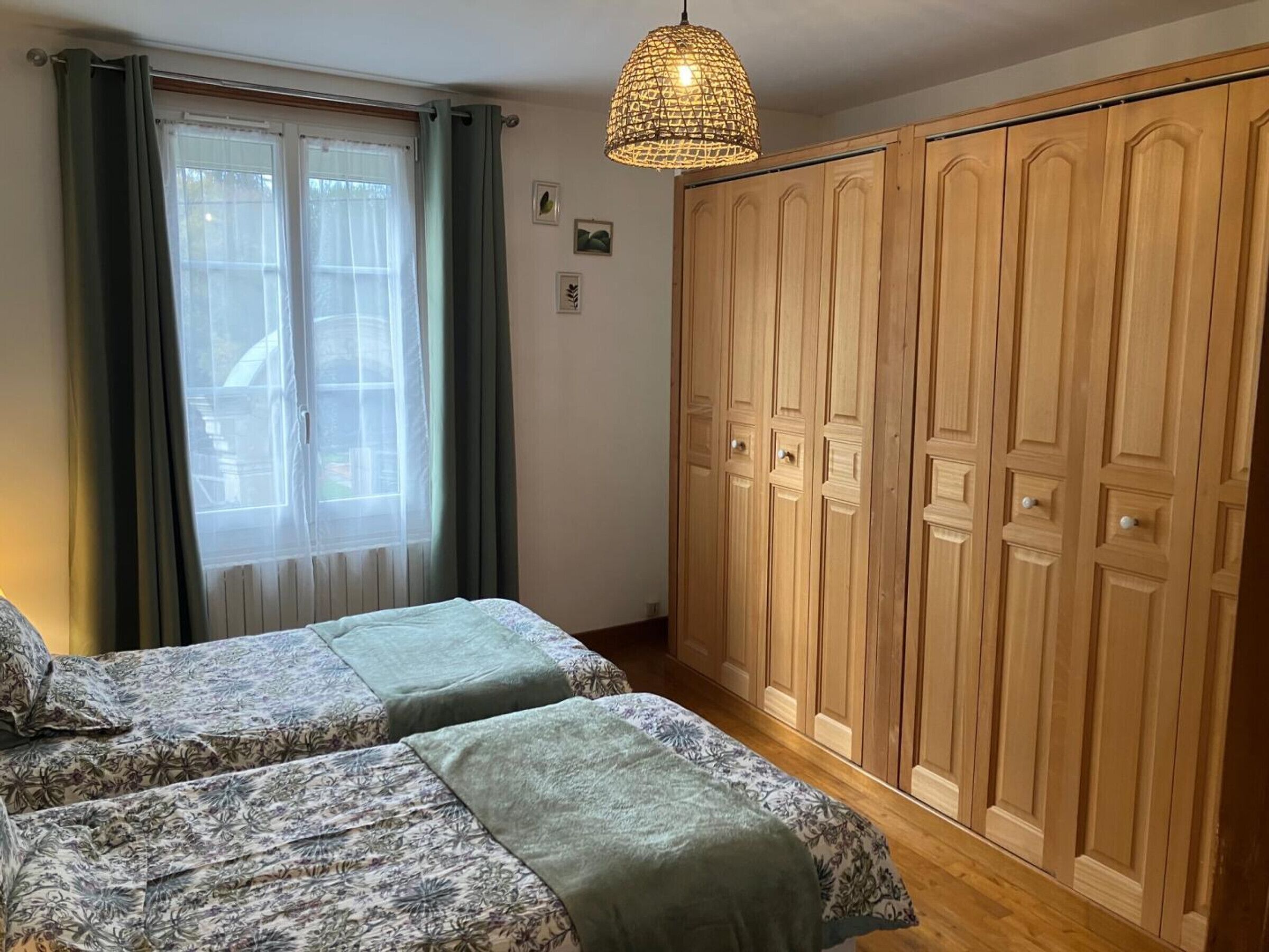 Une chambre avec deux lits, une grande armoire et un luminaire suspendu.