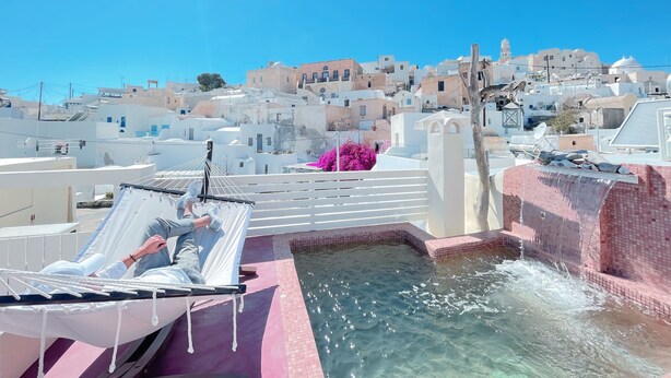 A rooftop pool with clear water, a hammock, and a view of white buildings in the background.
