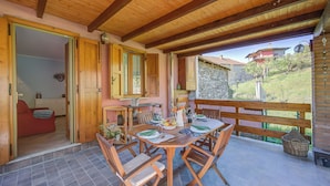 Uma sala de estar integrada com uma mesa de madeira posta para refeições, um sofá vermelho e vista para uma encosta.