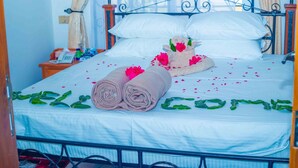 A neatly made bed with rolled towels and a decorative pillow, a bedside table with a phone, and a window with curtains. - LA'TONNA SAFARI HOTEL (Serengeti)