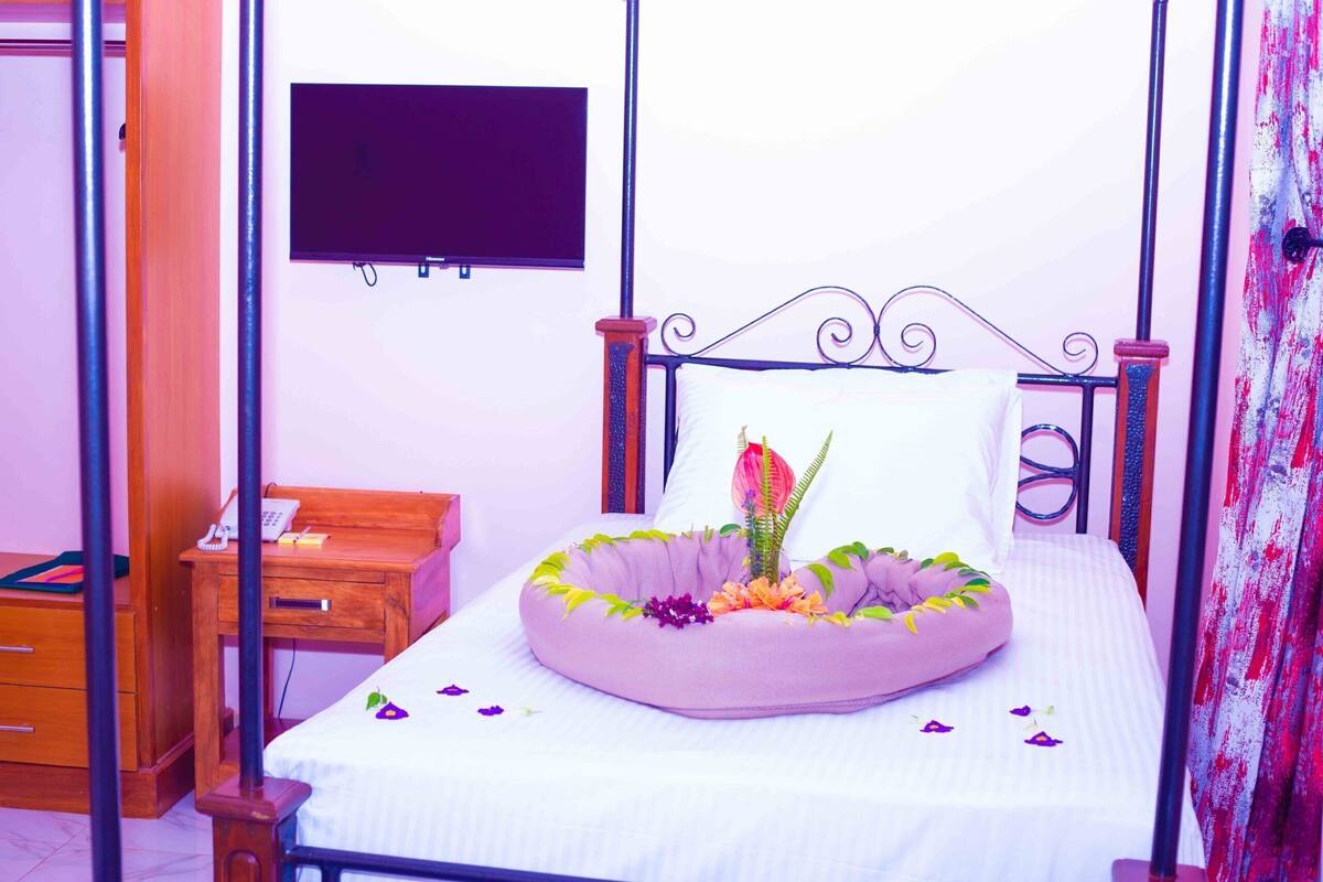 A bed with a decorative headboard, a bedside table with a telephone, and a wall-mounted TV.