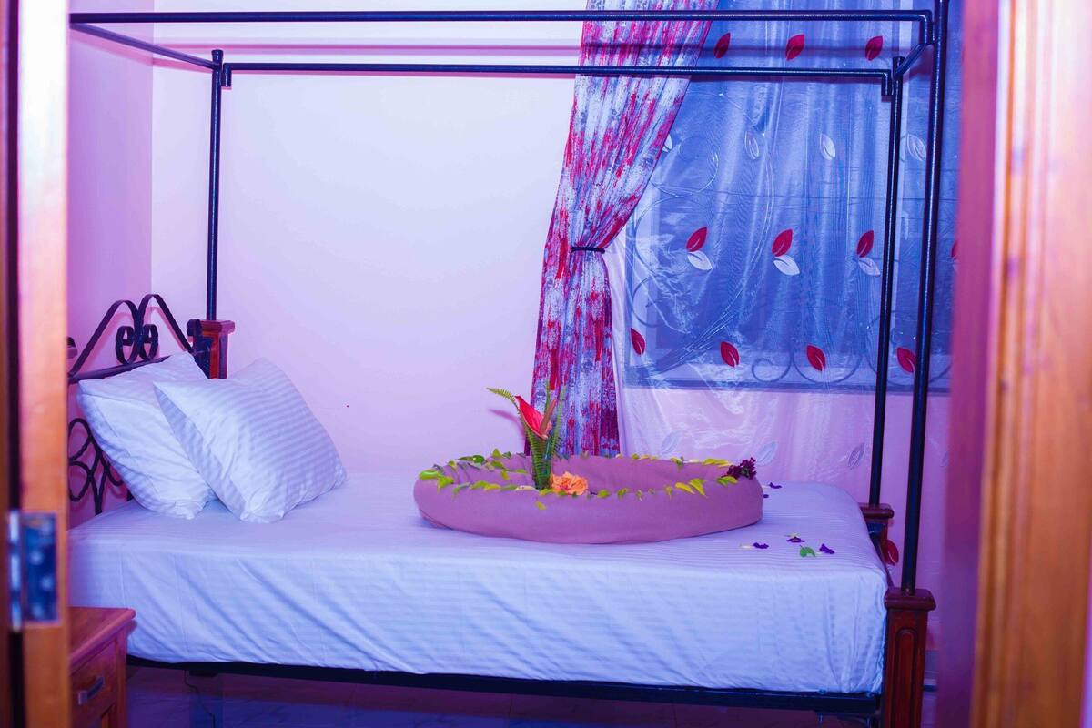 A four-poster bed with a canopy, white bedding, and a floral arrangement on the footboard.
