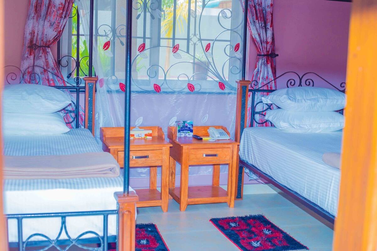 A bedroom with two beds, a small wooden desk, and a window with decorative metalwork.