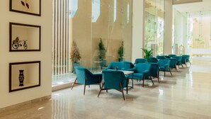 Un hall d’entrée moderne avec des fauteuils de couleur turquoise, un mur en verre et des œuvres d’art encadrées.