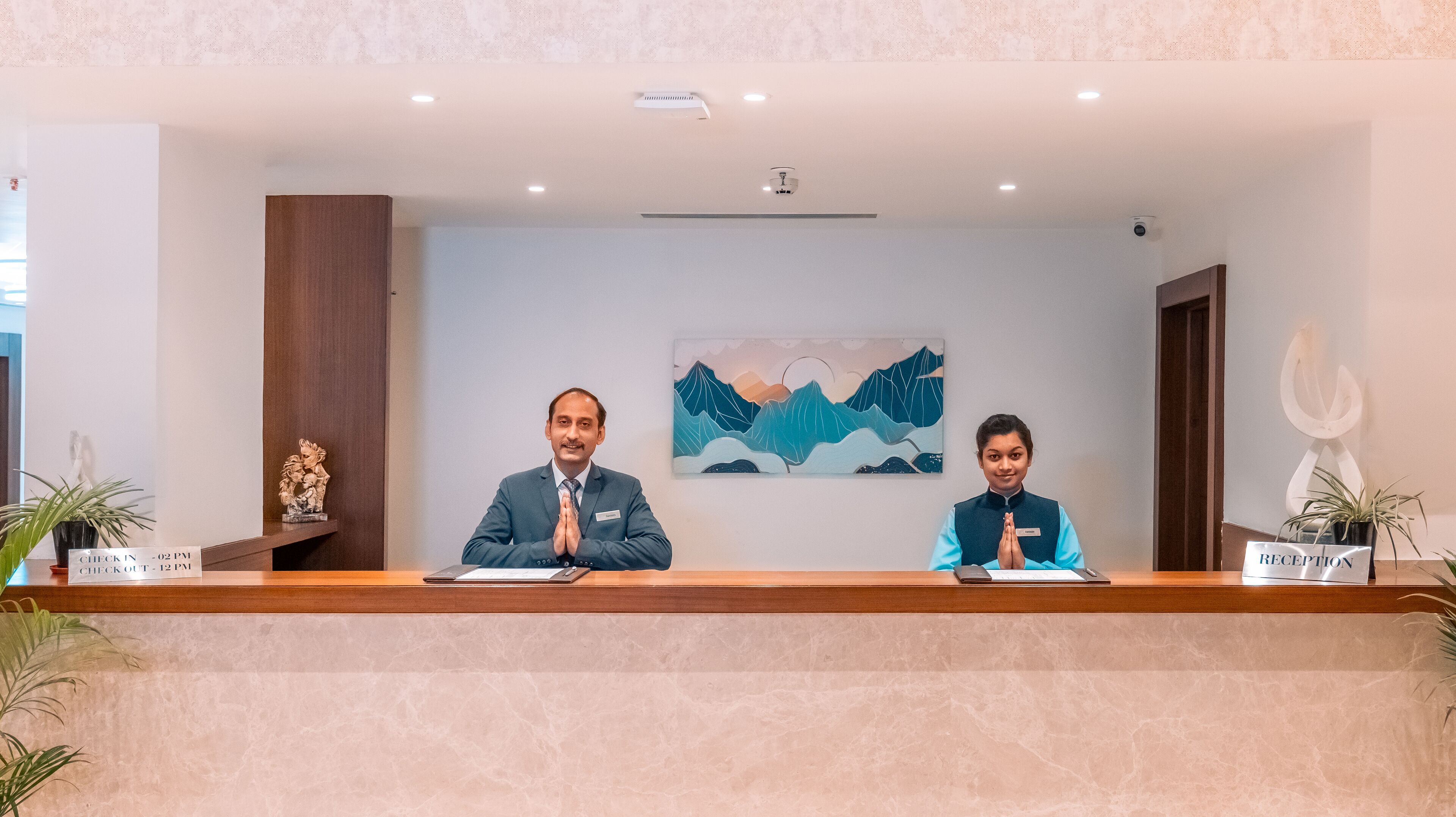 Una reception con due persone sedute, un quadro raffigurante montagne e la insegna della reception.