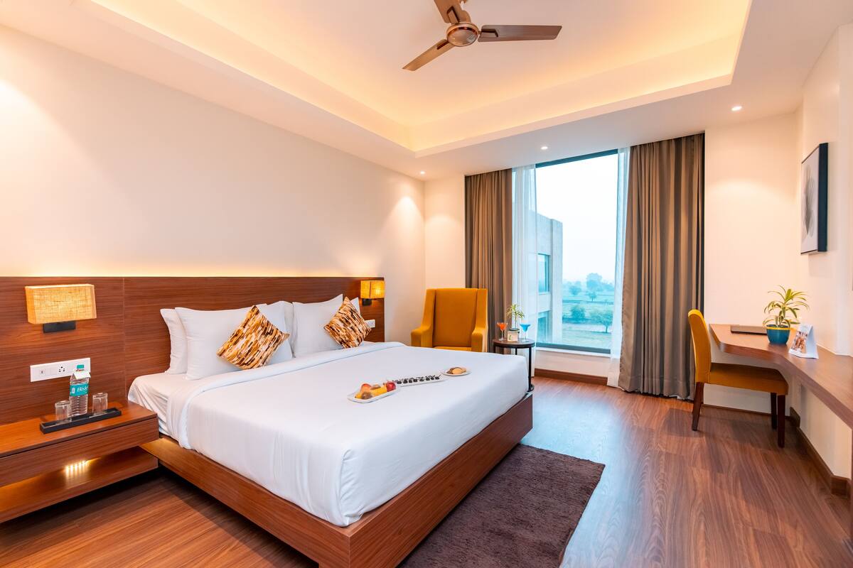 A modern hotel room with a large bed, a desk, a chair, and a view of the city.