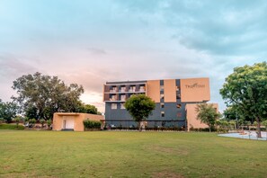A modern building with "The Fern" signage, surrounded by a well-maintained lawn and trees. - The Fern Alwar (Malakhera)