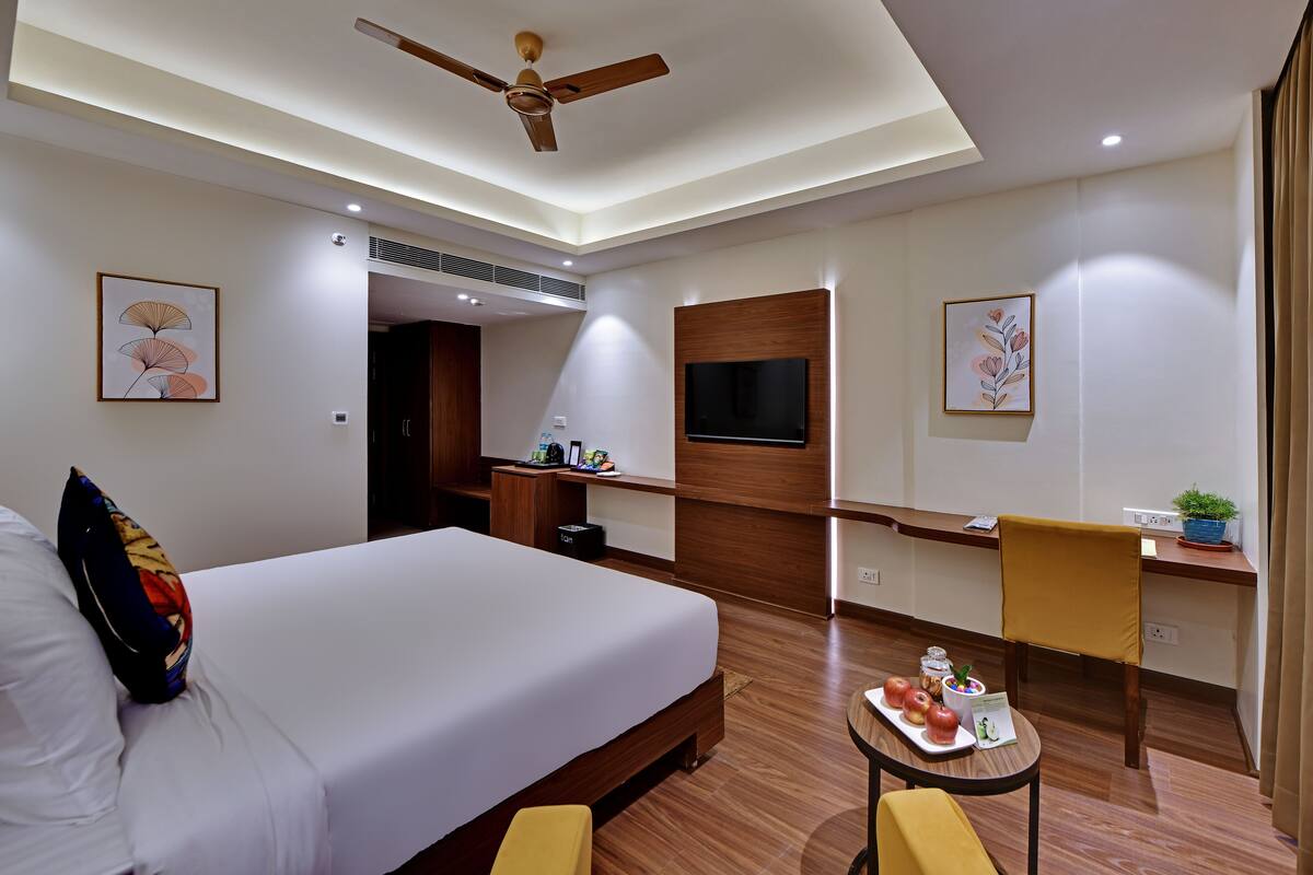 A hotel room with a large bed, a desk, a chair, a TV, and a ceiling fan.