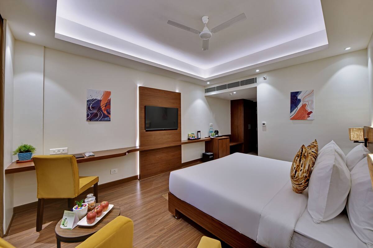 A modern hotel room with a large bed, a desk with a chair, a flat-screen TV, and artwork on the walls.
