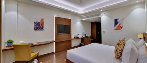 A modern hotel room with a large bed, a desk with a chair, a flat-screen TV, and artwork on the walls.