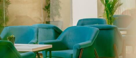 A modern indoor seating area with blue chairs and a small table, featuring a glass wall and a potted plant.