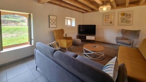 Ein modernes Wohnzimmer mit großem Fenster, Holzbalkendecke, Flachbildfernseher und einer Couch.