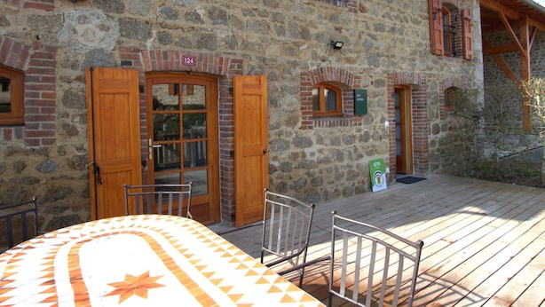 Ein Steinhaus mit hölzernen Fensterläden, einem Schild mit der Aufschrift Zimmer 124 und einer Terrasse mit Metallstühlen.