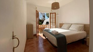 A bedroom with a bed, a wooden door, and a view of the outside.