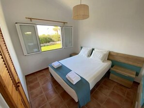 Ein Schlafzimmer mit Bett, einem Fenster mit Rollläden, einer Hängeleuchte und einer Holztür.