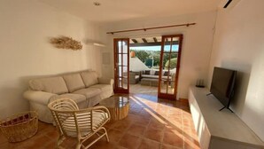 A living room with a sofa, a wicker chair, a TV, and a view through a glass door to an outdoor area.