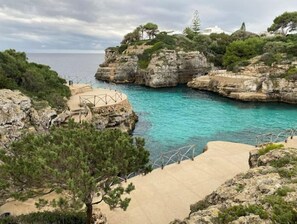 Eine Küstenlandschaft mit steilen Felsen, klarem türkisblauem Wasser und einem gepflasterten Weg zu einer Aussichtsplattform.