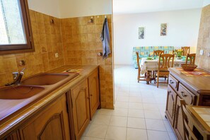 Een keuken met houten kastjes, een dubbele spoelbak en een eethoek met een tafel en stoelen.