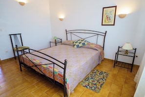 Une pièce comprenant un lit, deux tables de chevet, une chaise, un tapis et une lampe fixée au mur.