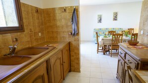 Een keuken met houten kastjes, een spoelbak en een eethoek met stoelen en een tafel.