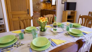 Een eettafel gedekt met groene borden, glazen en bestek, een vaas met bloemen, en een fles wijn.