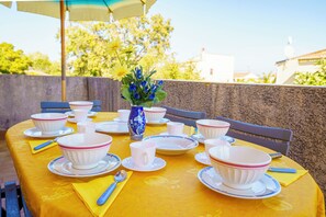 An outdoor dining setup with a yellow tablecloth, white and pink patterned bowls, cups, and a blue vase with flowers. - Charming 2-Bedroom Apartment 100m from the Beach Terrace Fiber WiFi  (Linguizzetta)