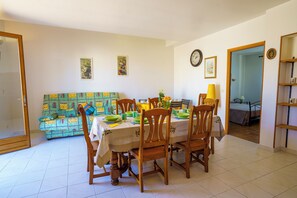 Un coin repas avec une table dressée pour quatre personnes, entourée de chaises, et un canapé et un lit visibles au fond.