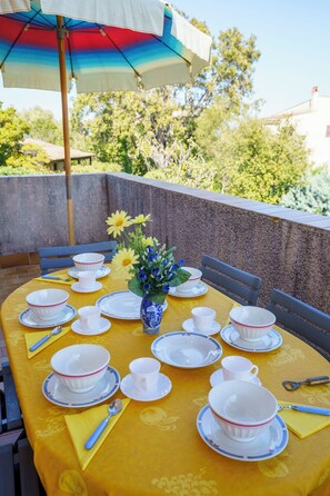 Un espace de restauration en plein air avec une table dressée pour le thé, entourée de chaises, et un parasol offrant de l’ombre.