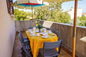 Een buitenterras met een tafel voor vier personen, omringd door stoelen, onder een gestreepte parasol.
