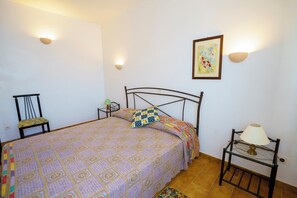 Een slaapkamer met een bed, een stoel, een nachtkastje, een lamp en een wandlamp.