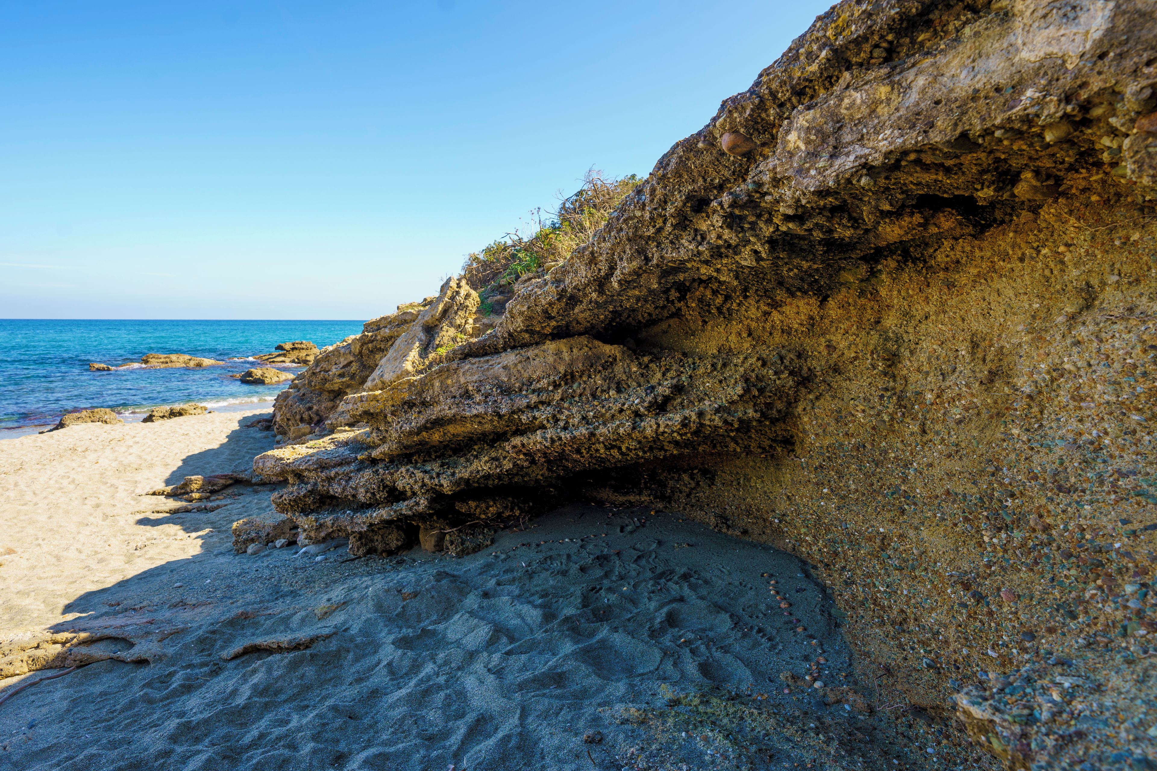 A rocky coastline with a sandy beach and clear blue sea.