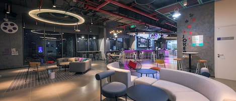 A modern lounge area with seating arrangements, a bar, and a visible exit sign.