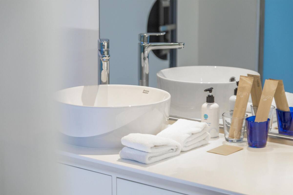 A bathroom with a large white sink, a mirror, a towel rack, and a glass of water.