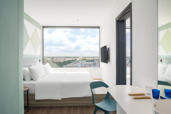 Una habitación de hotel moderna con un ventanal grande, una cama, un escritorio y una silla.