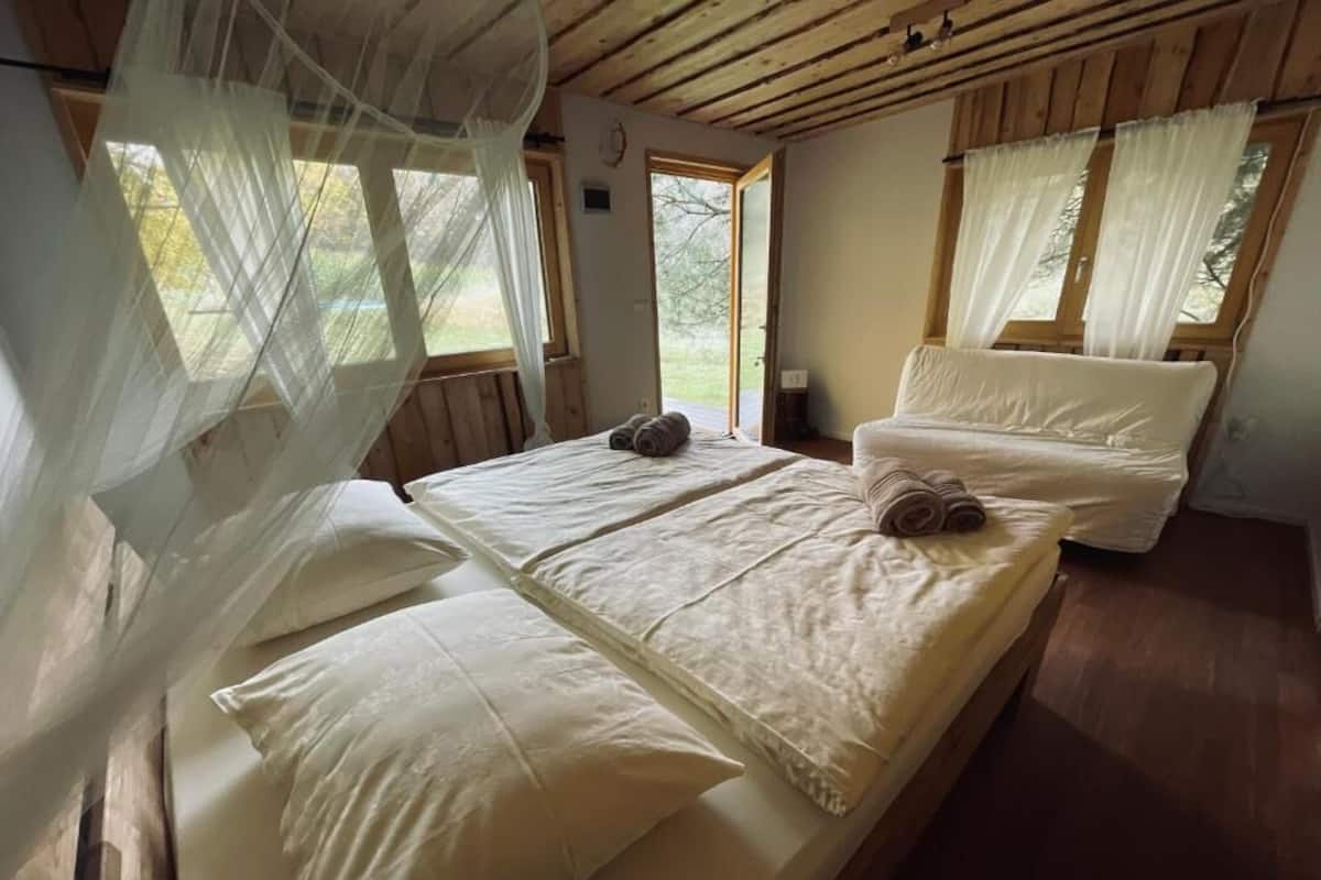 A bedroom with two beds, wooden floors, and large windows with curtains.