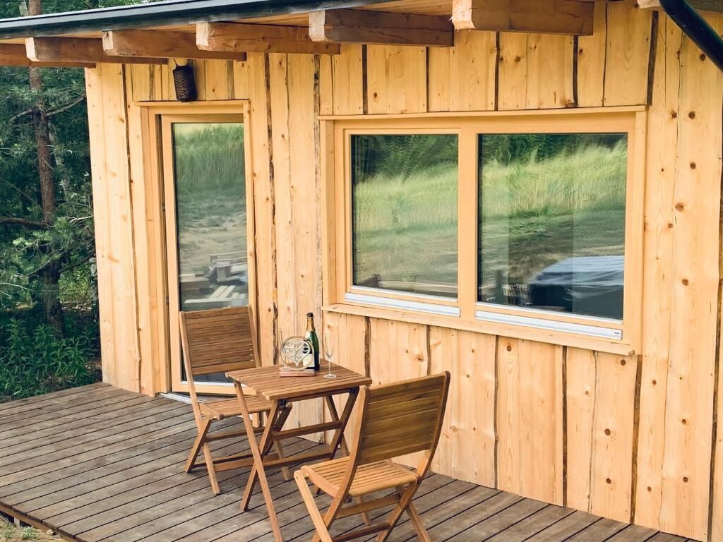 Una cabaña de madera con un porche, dos sillas, una mesa y una botella de vino.