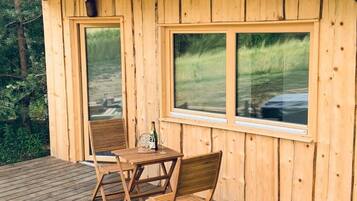 Una cabaña de madera con un porche, dos sillas, una mesa y una botella de vino.