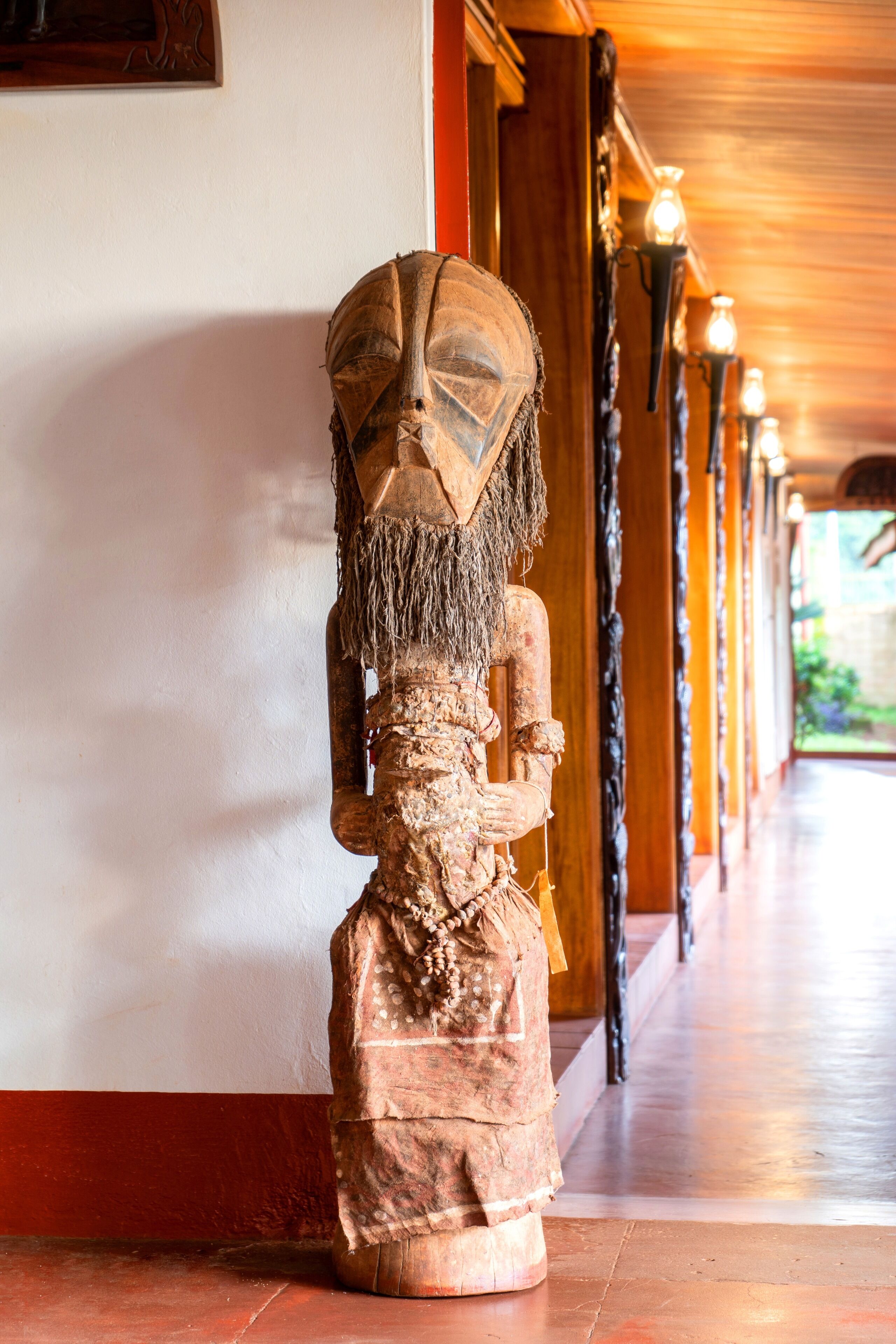 A wooden statue in a corridor with a tiled floor and a wooden ceiling.