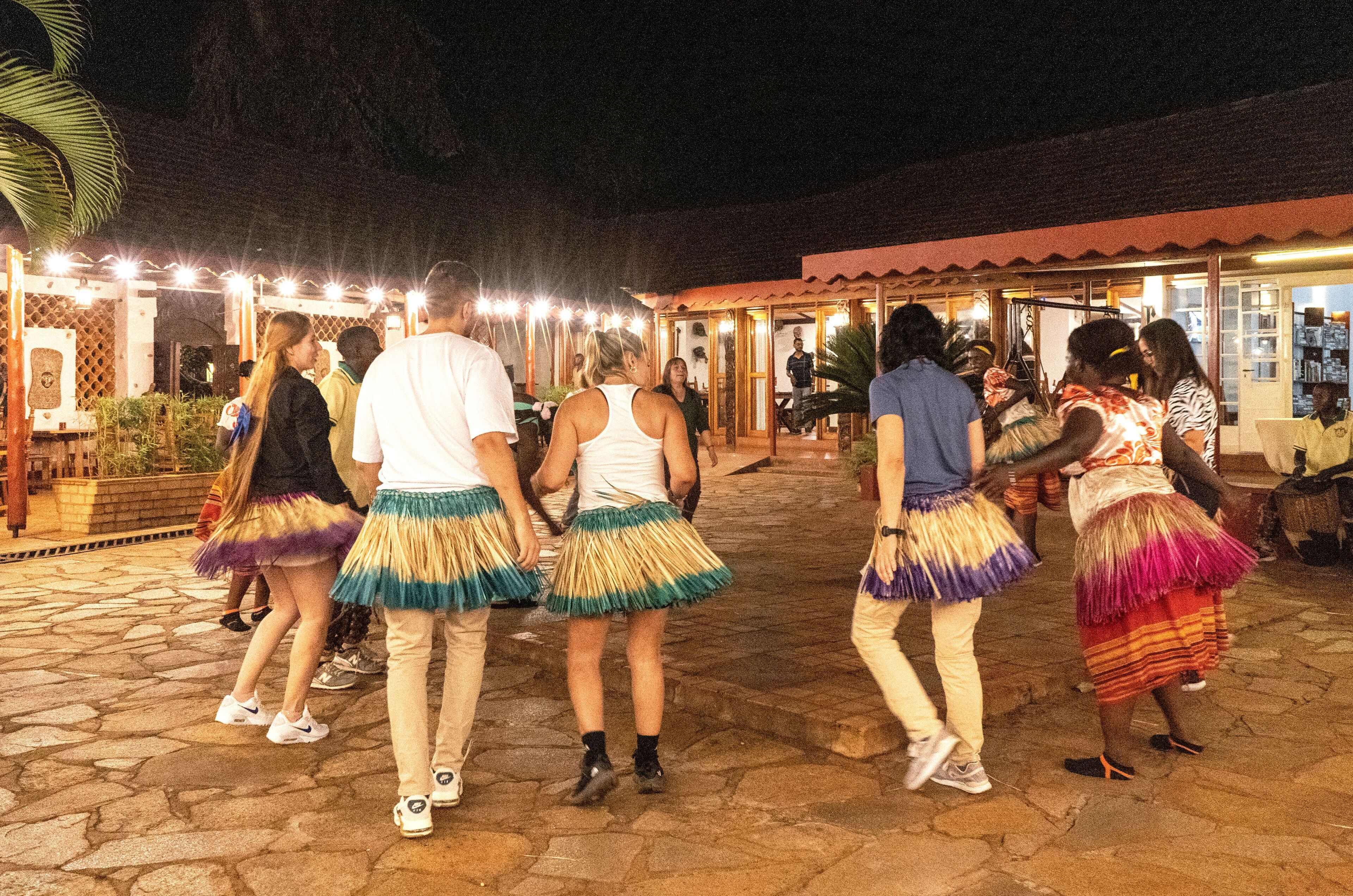 A group of people dancing in a courtyard with a stone floor and a building with a red roof in the background.