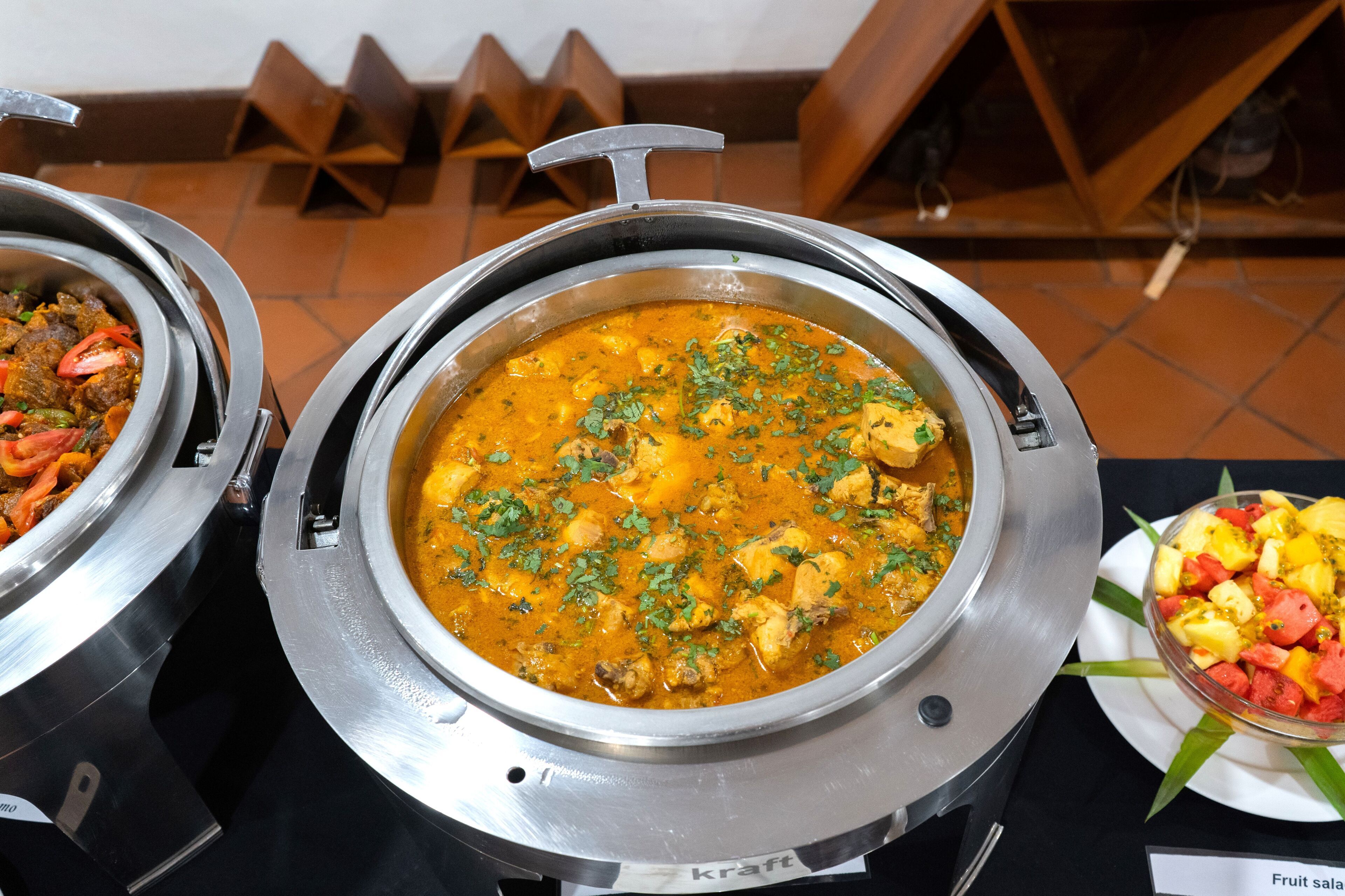 A buffet with a variety of dishes, including a curry and a fruit salad.