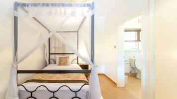 A four-poster bed with a canopy, a bedside table, a nightstand, and a view of the bathroom.