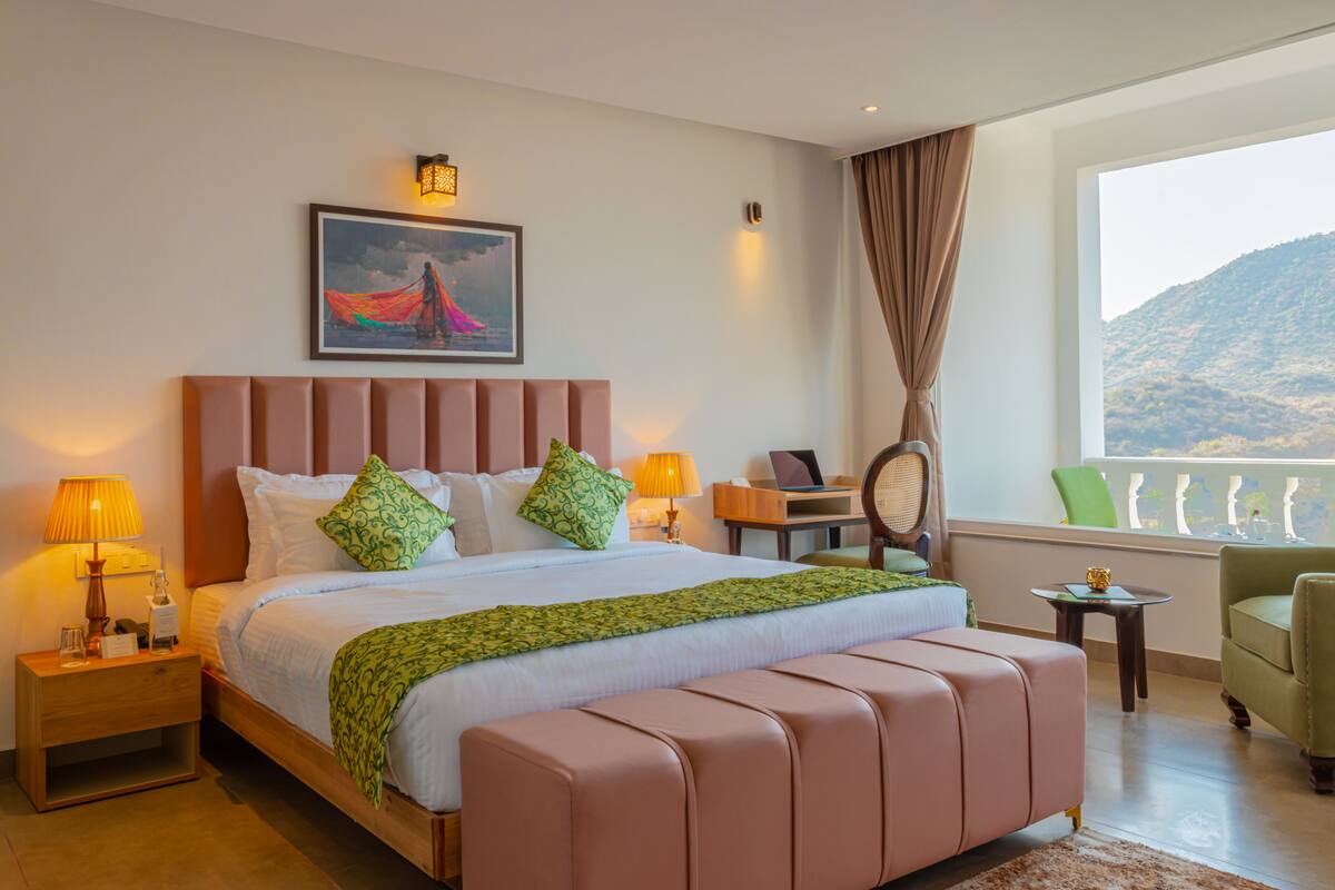 A hotel room with a large bed, a desk, a chair, a lamp, and a view of the outdoors.