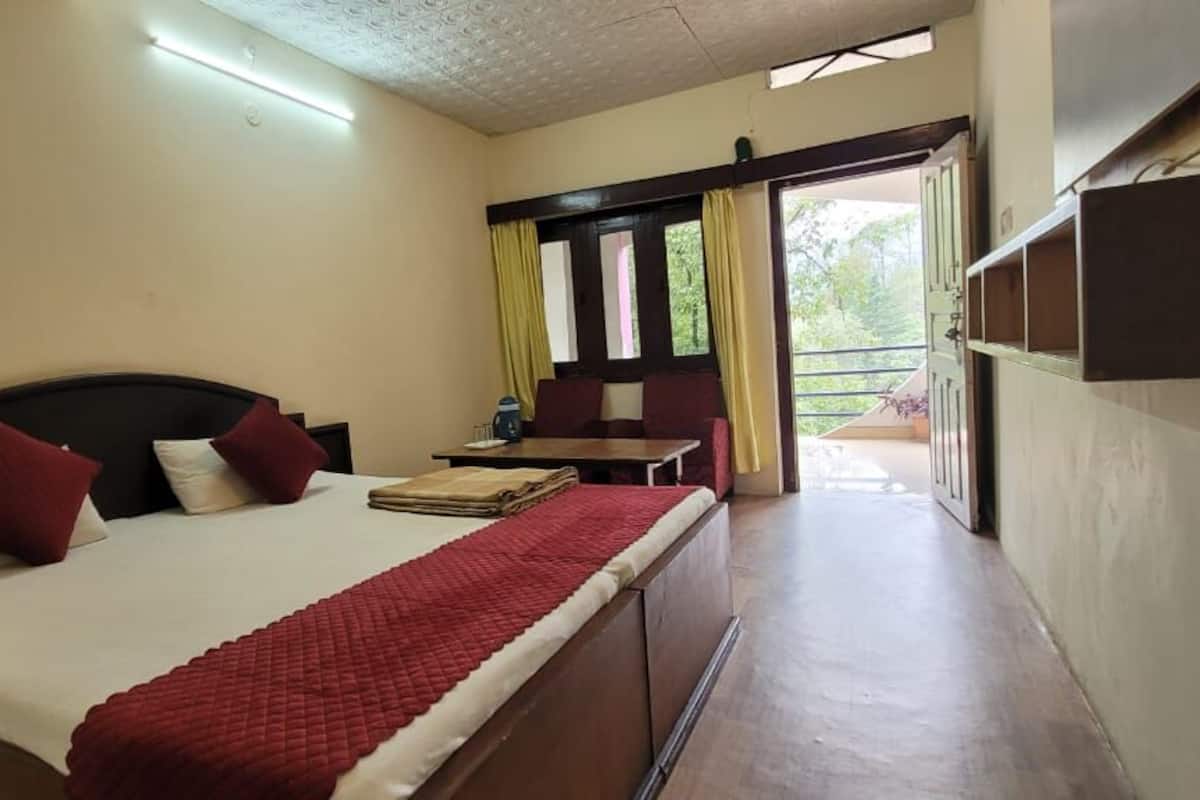 A hotel room with a bed, a small table, and a view of the outdoors.